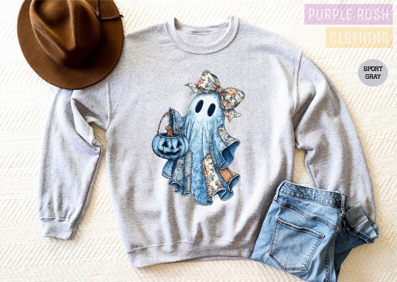 a gray sweatshirt with a graphic of a ghost wearing a bow and holding a pumpkin, along with a brown hat and a pair of blue jeans.