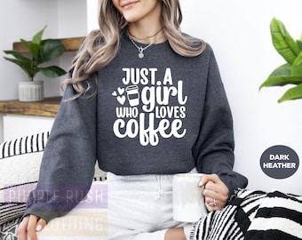 May include: A dark heather grey sweatshirt with the text "Just a girl who loves coffee" in white. A white coffee cup with a heart is shown next to the text.