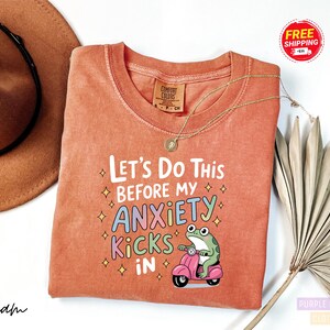 a red t-shirt with a humorous text and an illustration of a frog riding a motorcycle.