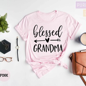 May include: Pink t-shirt with the text "blessed grandma" in black lettering with an arrow and heart graphic.