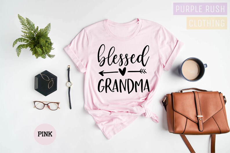 May include: Pink t-shirt with the text "blessed grandma" in black lettering with an arrow and heart graphic.
