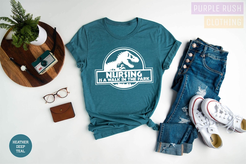 May include: A teal blue t-shirt with a white graphic of a dinosaur and the text "Nursing is a walk in the park".