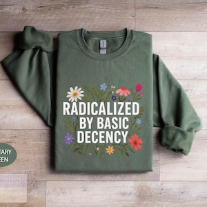 A green sweatshirt with a printed design on it, featuring the text "RADICATED BY BASIC DECENCY" surrounded by colorful flowers.