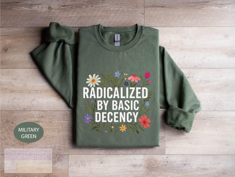 A green sweatshirt with a printed design on it, featuring the text "RADICATED BY BASIC DECENCY" surrounded by colorful flowers.