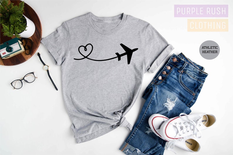 May include: A grey t-shirt with a black airplane and heart design. The text "Purple Rush Clothing" and "Athletic Heather" is visible in the image.