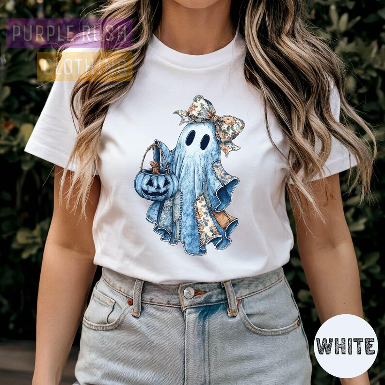 A woman wearing a white t-shirt with a graphic of a ghost holding a pumpkin and a bow.
