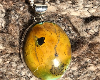 May include: A silver chain necklace with a pendant featuring a large oval-shaped green and brown stone with black and white veins.