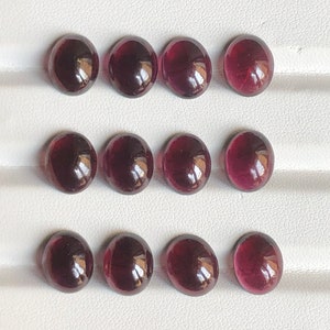 Könnte beinhalten: Zwölf runde, cabochon geschliffene, tiefrote Edelsteine. Die Edelsteine sind in drei Reihen zu vier angeordnet.
