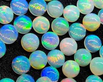 May include: A collection of iridescent, round opal gemstones. The opals display a range of colors, including blue, green, and pink, with a shimmering effect. The gemstones are scattered on a black surface.