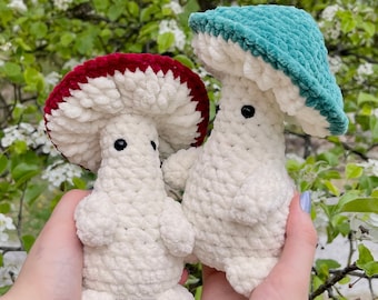 May include: Two crocheted mushroom plushies, one with a red and white cap and the other with a teal cap. Both have white bodies and black eyes.