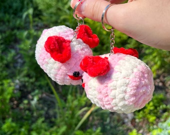 May include: Two pink and white crocheted fluffy keychains with red bows and black eyes. The keychains are attached to silver key rings.