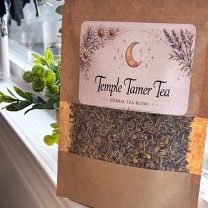 以下が含まれることがあります： テンプルテイマーティーの茶色の紙袋、ハーブティーブレンド。ラベルには三日月と花の模様が描かれています。袋の底には、お茶の葉とカモミールの花が見える透明な窓があります。