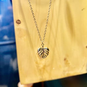 May include: A gold necklace featuring a delicate, cutout monstera leaf pendant.