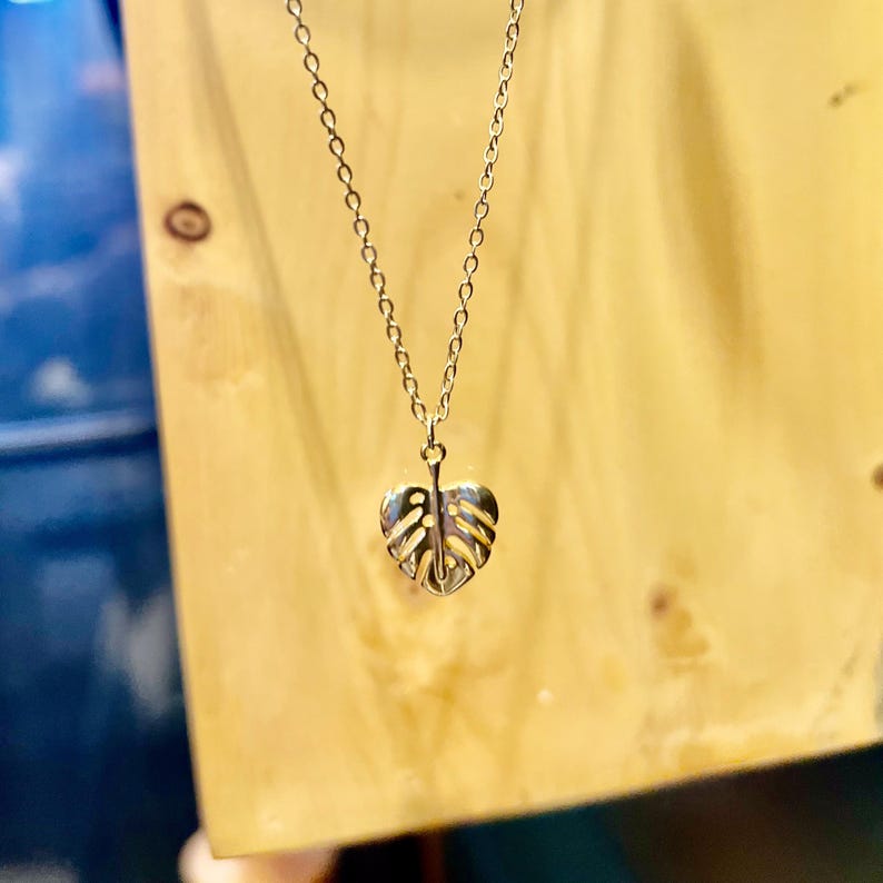 May include: A gold necklace featuring a delicate, cutout monstera leaf pendant.