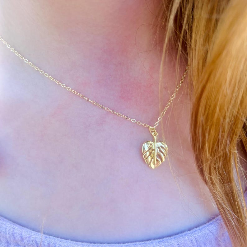 May include: A gold necklace featuring a delicate chain and a pendant in the shape of a monstera leaf.
