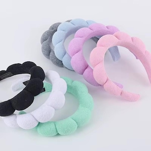 May include: A collection of seven padded headbands featuring a scalloped, cloud-like design. The headbands are available in a variety of solid colors including black, white, mint green, light blue, lavender, pink, and dark gray fabric textures.