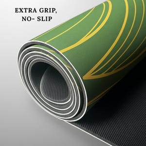 May include: Rolled-up yoga mat with a green surface and yellow curved lines. The mat has a black underside and white edges. Text on the mat reads "EXTRA GRIP, NO-SLIP".