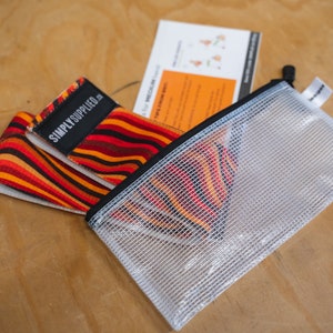 May include: A set of resistance bands with a vibrant orange, red, and brown striped pattern. The bands are labeled "SIMPLY SUPPLIED." They are accompanied by a clear mesh zipper pouch and a small instruction card. The items are on a wooden surface.