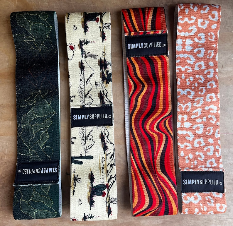 May include: Four resistance bands with unique patterns. One is dark green with gold lines, another has a desert landscape design, a third features red and orange wavy stripes, and the last has a leopard print. Each band has a black label with "SIMPLY SUPPLIED.CO".