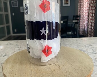 May include: A glass jar with a bamboo lid, filled with white tissue paper and red flowers. The jar has a blue and white design with a white star on it.