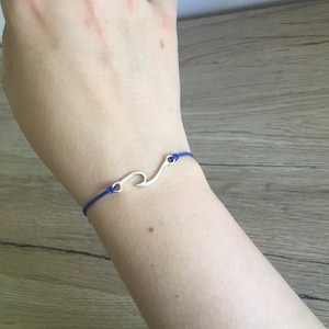 Könnte beinhalten: Ein blaues Armband aus Schnur mit einem silbernen Wellen-Anhänger.