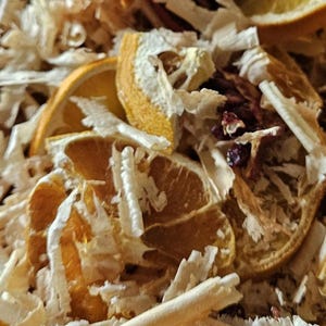 Op de afbeelding: Close-up van gedroogde sinaasappelschijfjes en houtsnippers. De sinaasappelschijfjes hebben een levendige oranje kleur, waarbij sommige de textuur van de vrucht laten zien. De houtsnippers zijn lichtbeige van kleur en creëren een getextureerde achtergrond.