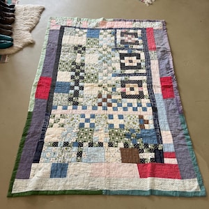 May include: A handmade quilt with a patchwork design. The quilt features a variety of fabrics in shades of blue, green, pink, and brown. The quilt has a rectangular shape and is likely used for bedding or decoration.
