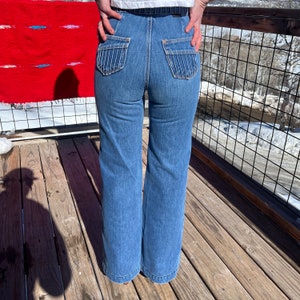 May include: A pair of blue denim jeans with a high waist and wide legs. The jeans have decorative stitching on the back pockets.