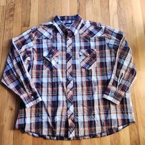 Puede incluir: Una camisa de cuadros de manga larga en tonos azules, rojos, naranjas y blancos. La camisa tiene dos bolsillos en el pecho con cierre de botón y una parte delantera abotonada. El cuello es puntiagudo y los puños tienen cierres de botón.