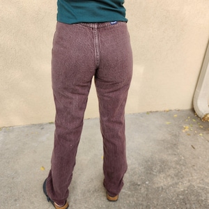 Op de afbeelding: Een bordeauxrode jeans met een klassiek ontwerp met vijf zakken. De jeans heeft een rechte pijp en een vervaagde, getextureerde uitstraling. Het Wrangler-logo is zichtbaar op de achterzak.