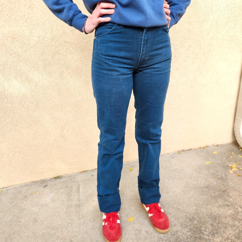 May include: Dark blue denim jeans with a high waist and straight leg. The jeans are paired with red sneakers with white stripes and a blue sweatshirt. The jeans have a classic five-pocket design.