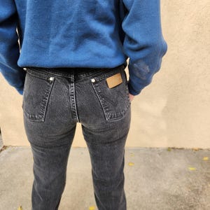 May include: Black denim jeans with a faded wash, featuring classic five-pocket styling and a leather patch on the back. The jeans are worn with a blue sweatshirt.