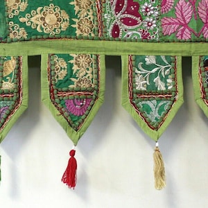 Puede incluir: Un tapiz de pared textil verde y dorado con bordados florales y estampados de cachemira. El tapiz tiene una serie de colgantes decorativos con borlas en varios colores, incluyendo verde, rojo y naranja. El diseño es intrincado y colorido.