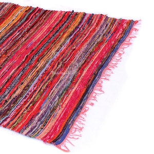 May include: A colorful, striped rug with a mix of red, orange, pink, and blue hues. The rug has a fringed edge and a woven texture. The rug is made of fabric strips and is suitable for home decor.