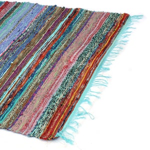 May include: A colorful, striped rag rug with a turquoise fringe. The rug features a variety of colors including red, blue, purple, and green. The rug is made of woven fabric.