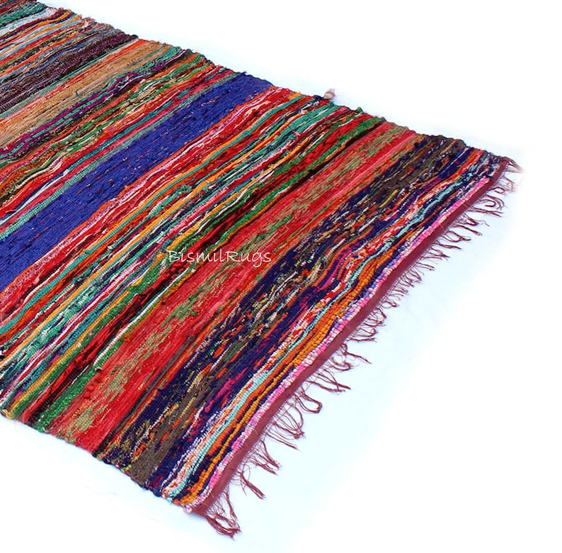 May include: A colorful, striped rug with a variety of colors including red, blue, green, and orange. The rug has a fringed edge and the text "BismilRugs" is visible. The rug is made of woven fabric.