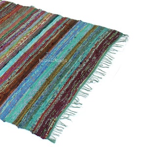 May include: A colorful, striped rag rug with a variety of colors including teal, burgundy, brown, and blue. The rug has a fringed edge and is made of woven fabric strips. The rug is angled, showing the diagonal stripes.