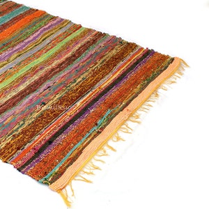 May include: A colorful, striped rug with a variety of colors including orange, green, purple, and brown. The rug has a fringed edge and is made of woven fabric. The rug is ideal for adding a pop of color to any room.