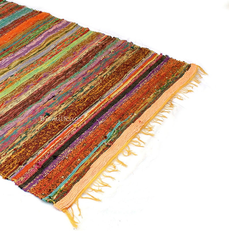 May include: A colorful, striped rug with a variety of colors including orange, green, purple, and brown. The rug has a fringed edge and is made of woven fabric. The rug is ideal for adding a pop of color to any room.
