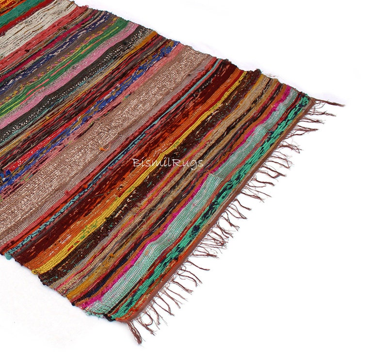 May include: A colorful, striped rug with a variety of colors including red, orange, green, and brown. The rug has a fringed edge and the text "Bismil Rugs" is visible. The rug is made of woven fabric.