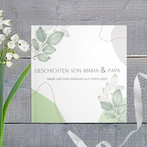 Könnte beinhalten: Ein weißes Buch mit einem grünen und braunen floralen Design. Der Titel des Buches lautet "Geschichten von Mama & Papa" und der Untertitel lautet "Mama und Papa erzählen aus ihrem Leben".
