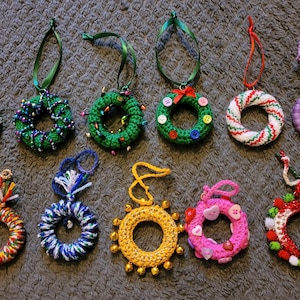May include: Twelve crocheted Christmas ornaments in various colors and designs, including wreaths, a snowflake, and a candy cane. The ornaments are all handmade and feature different embellishments, such as beads, buttons, and yarn.