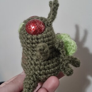 May include: A green crocheted plush toy with red glitter eyes and a green crocheted wing.