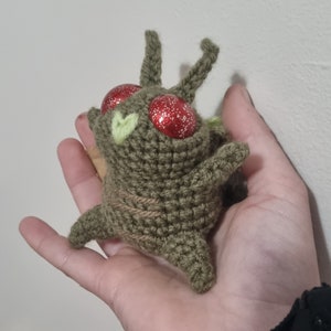 May include: A crocheted green and brown plush toy with red glitter eyes. The toy has two small green leaves on its head.