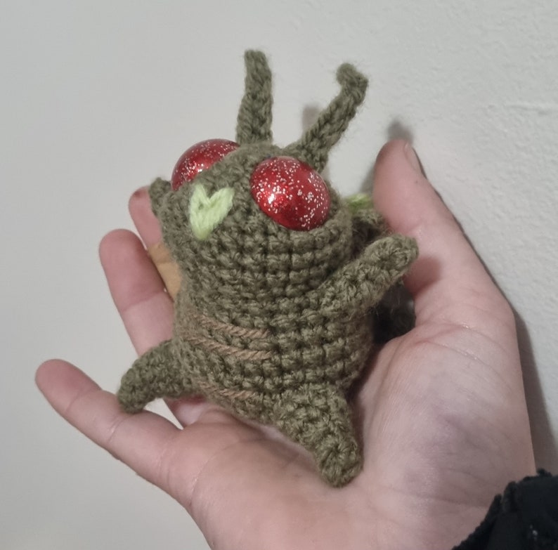 May include: A crocheted green and brown plush toy with red glitter eyes. The toy has two small green leaves on its head.