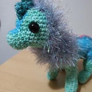 May include: A crocheted unicorn toy with a blue, green, and pink color gradient. The unicorn has a silver sparkly mane and a black button eye.