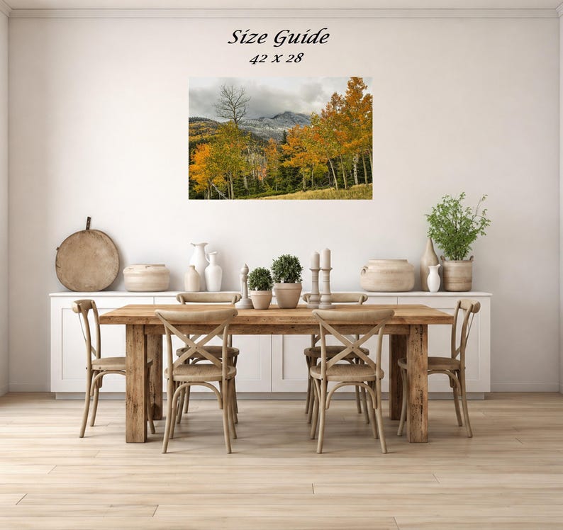 Mockup of a 42 by 28 inch autumn mountain landscape print displayed on a dining room wall above a wooden table.