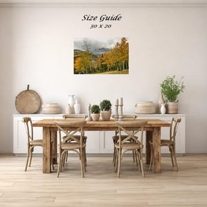 Mockup of a 30 by 20 inch autumn mountain landscape print displayed on a dining room wall above a wooden table.