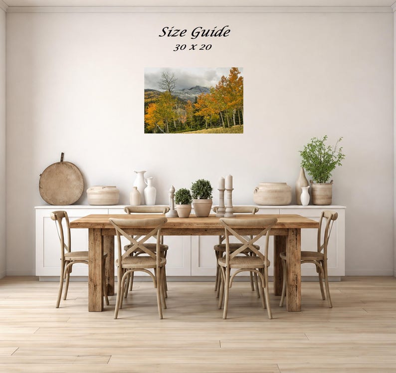 Mockup of a 30 by 20 inch autumn mountain landscape print displayed on a dining room wall above a wooden table.