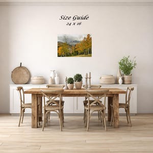 Mockup of a 24 by 16 inch autumn mountain landscape print displayed on a dining room wall above a wooden table.
